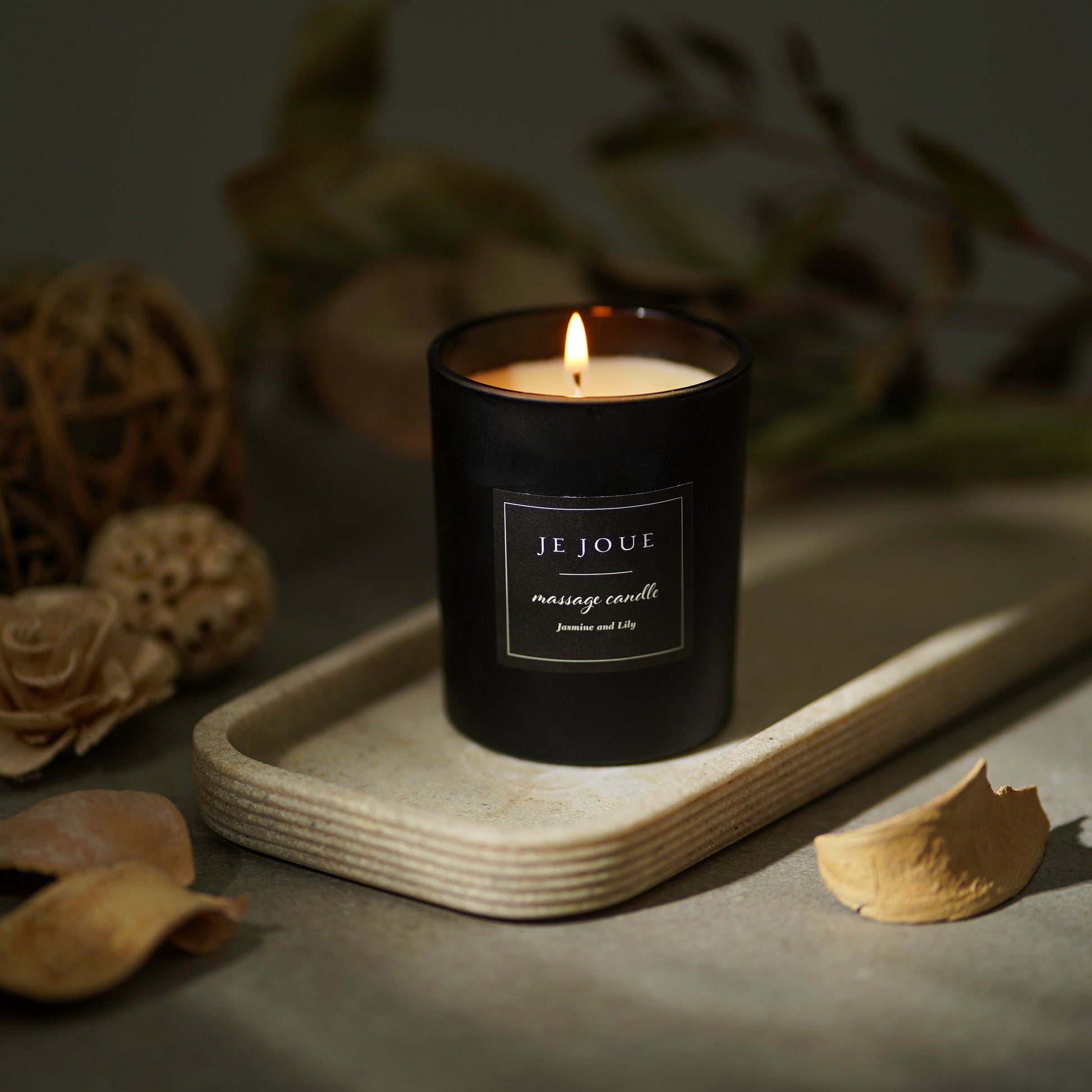 A lit black massage candle with a "Jasmine & Lily" label sits on a textured tray.