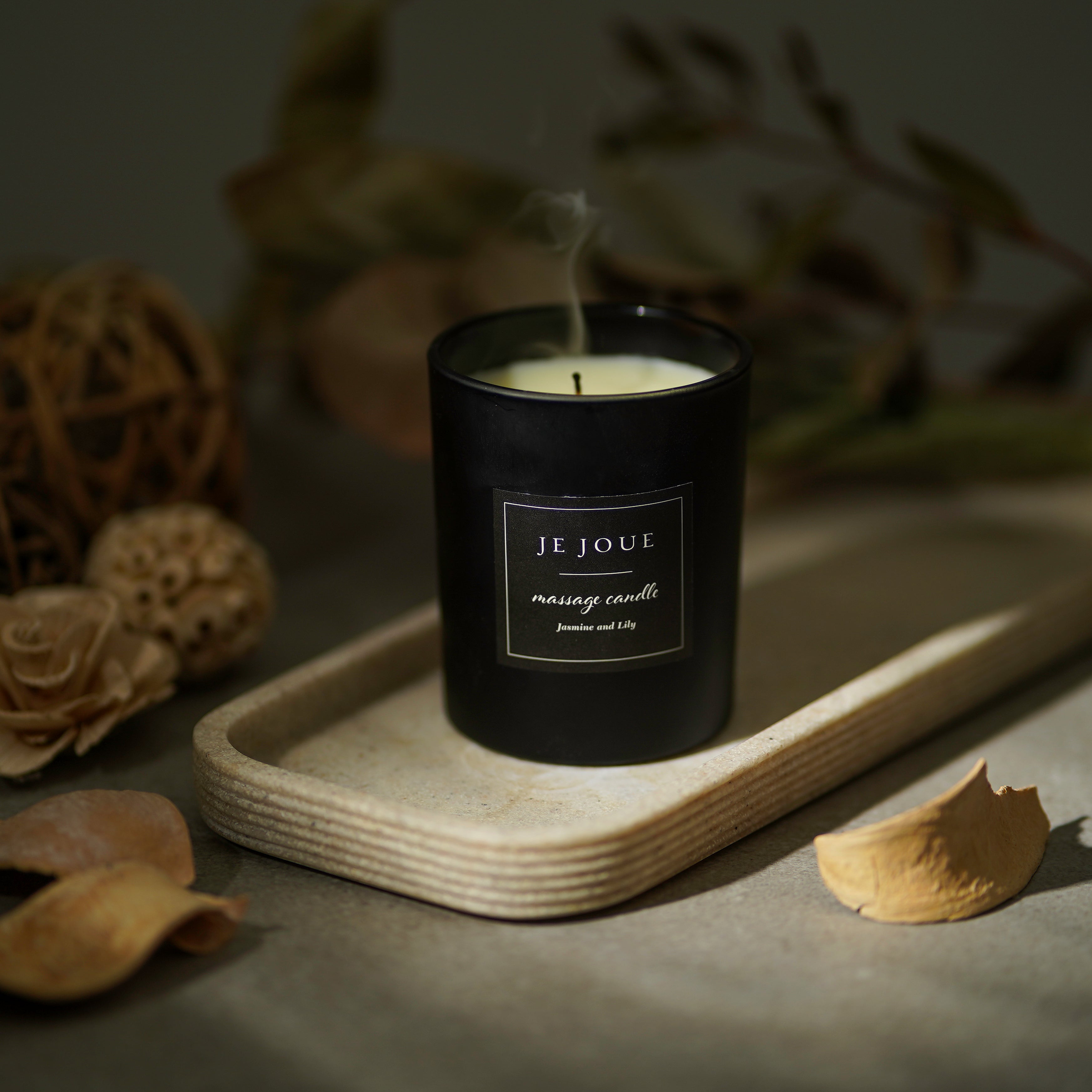 A black Je Joue massage candle with a label reading "Jasmine and Lily" sits on a tray.