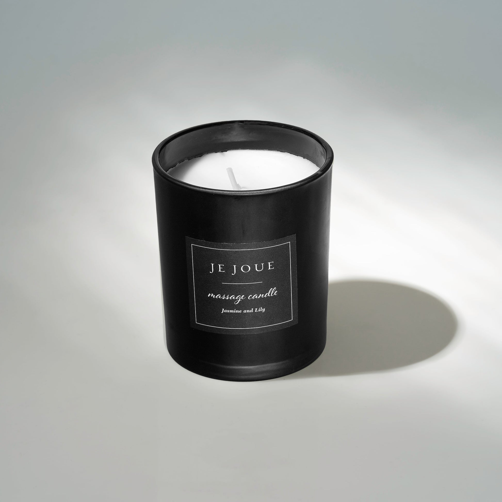 A black Je Joue massage candle with a white wax fill and a label reading "Jasmine and Lily".