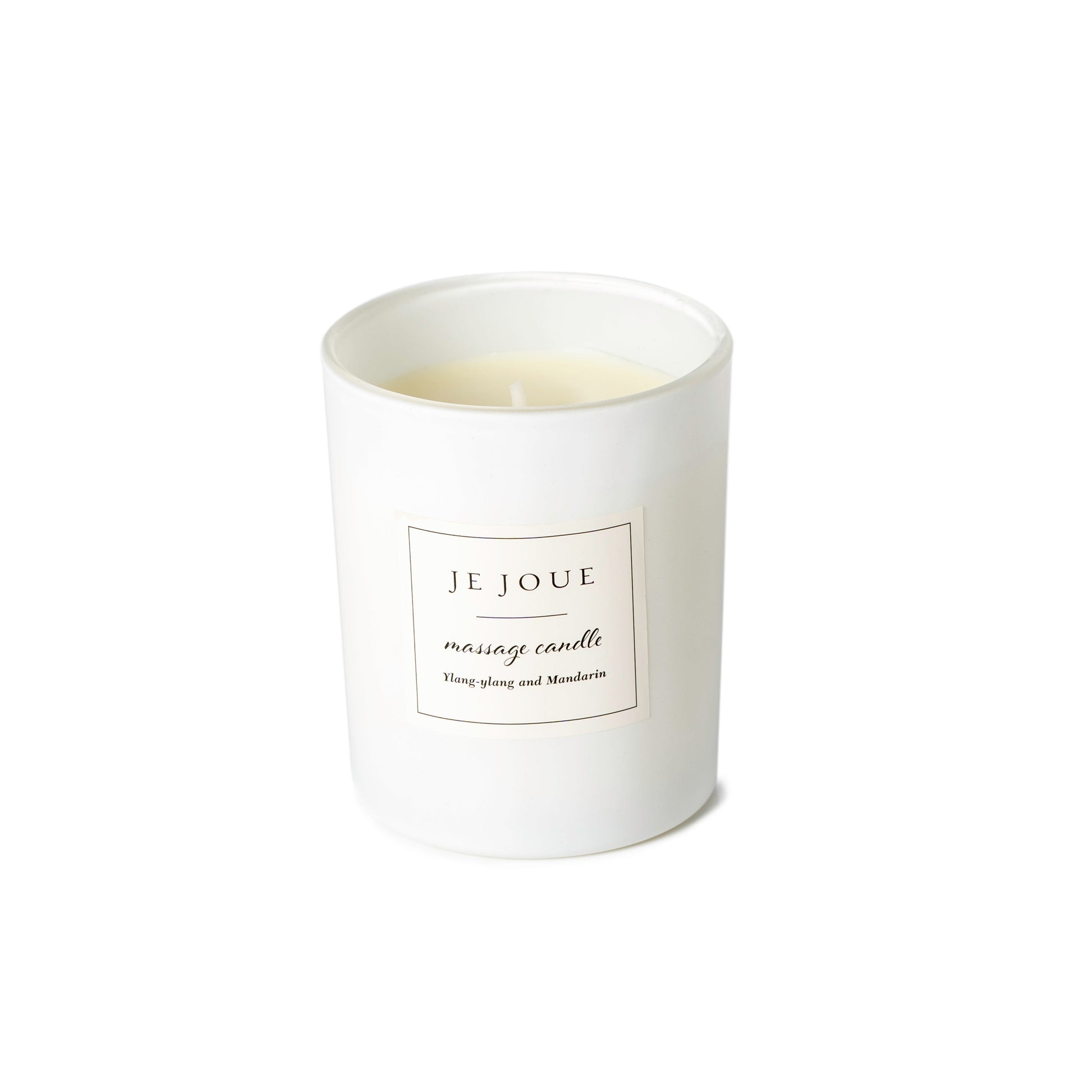 A white glass massage candle with a label that reads "JE JOUE massage candle Ylang-ylang and Mandarin".