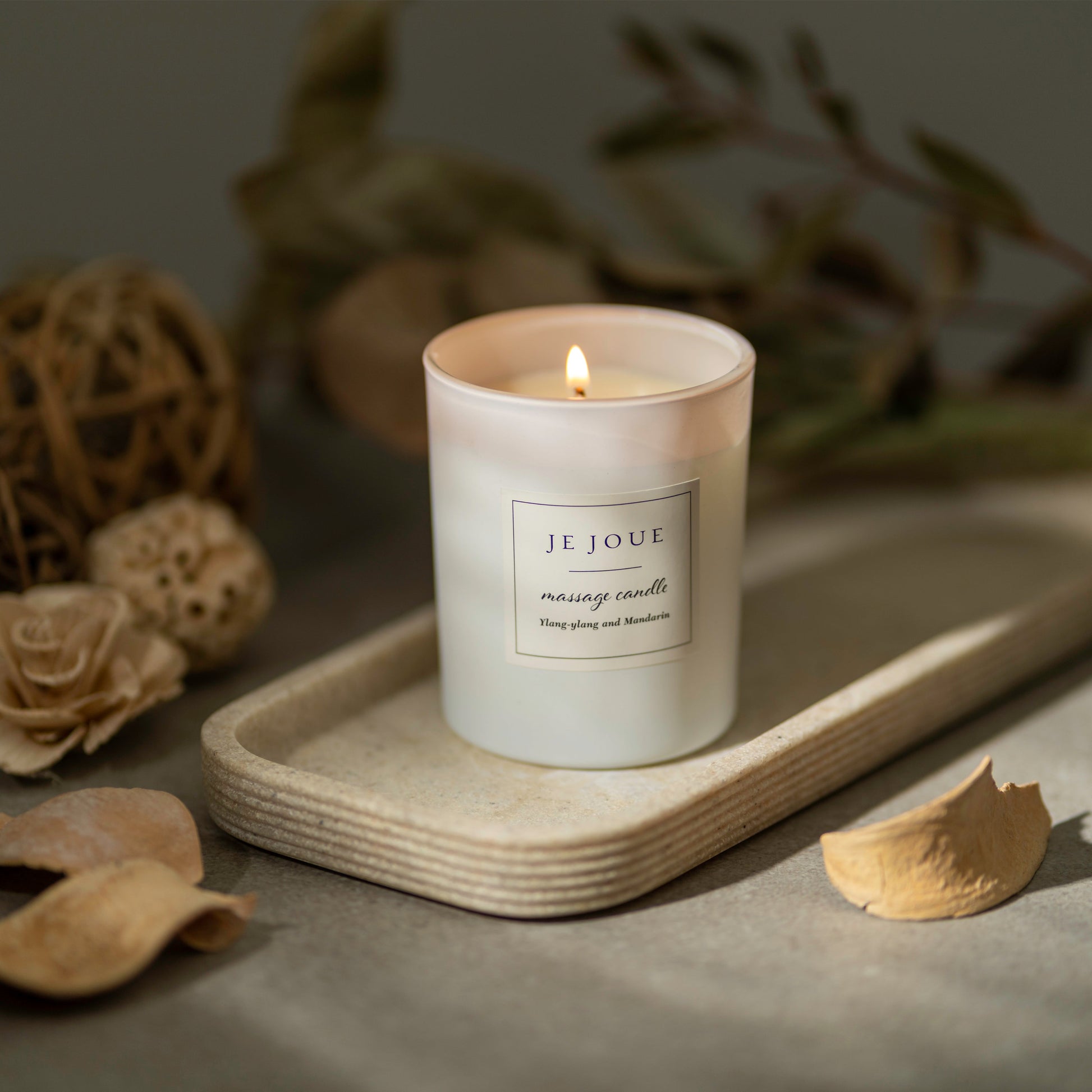 A lit Je Joue massage candle with Ylang Ylang and Mandarin scent.