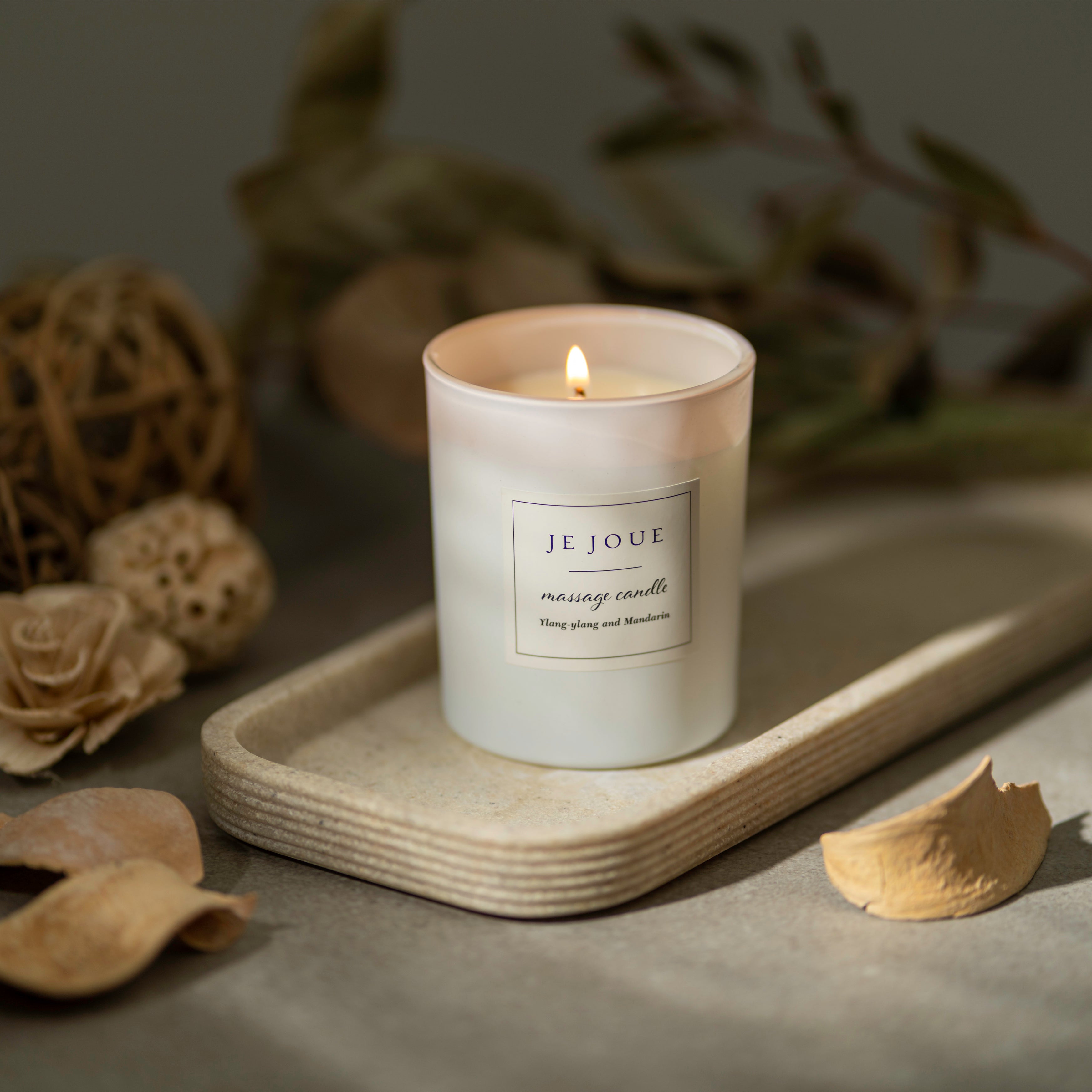 A lit Je Joue massage candle with Ylang Ylang and Mandarin scent.