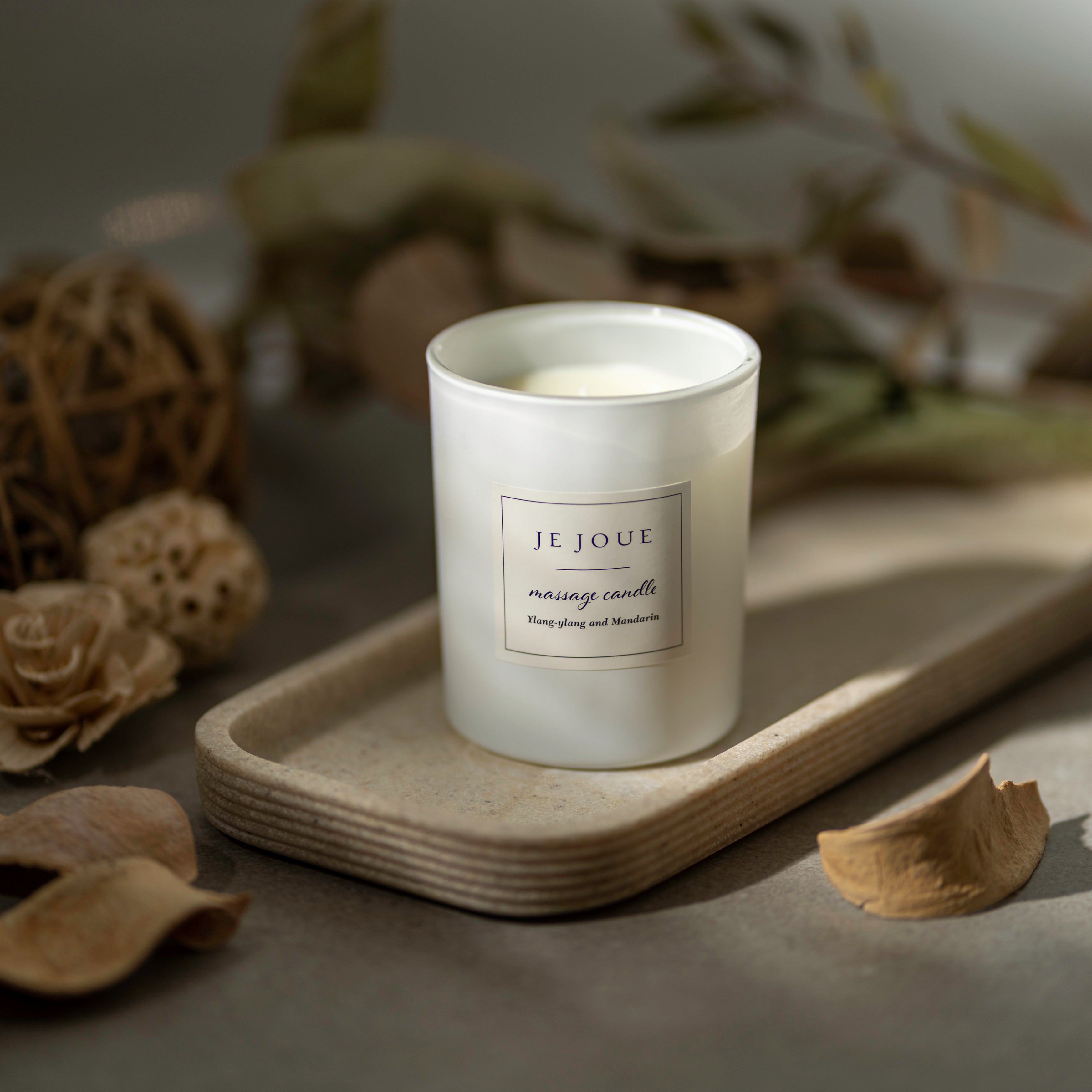 A white Je Joue massage candle with a label reading "Ylang-ylang and Mandarin" sits on a tray.
