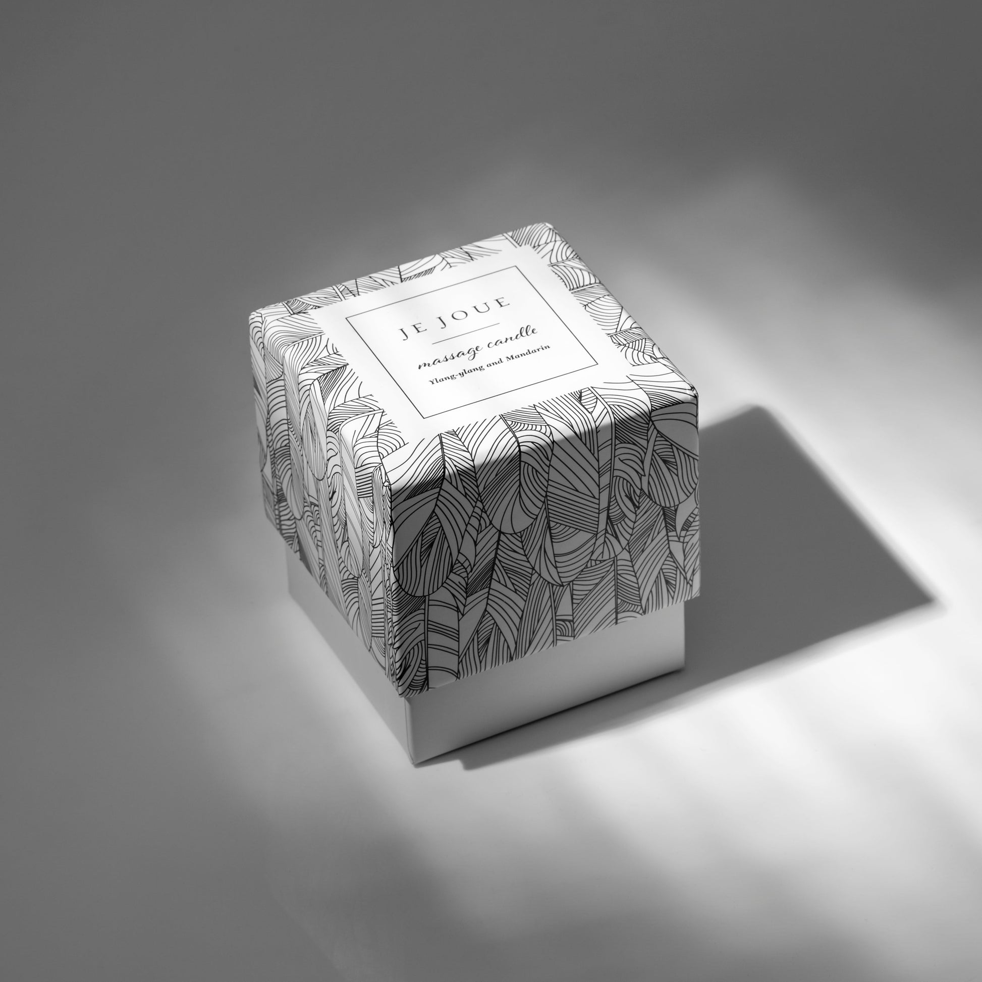 A Je Joue massage candle with a black and white leaf pattern and Ylang-ylang and Mandarin scent.