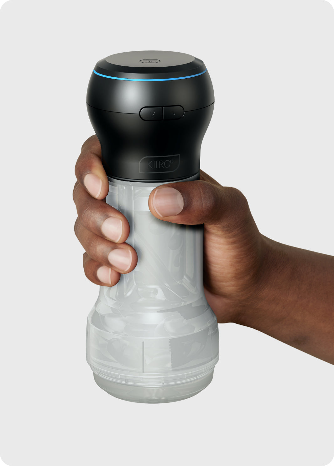 A hand holds a black and clear Kiiroo suction stroker with a blue light ring.