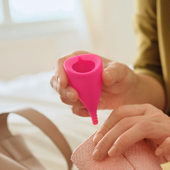 A pink Lily Cup menstrual cup is held by a person's hands.