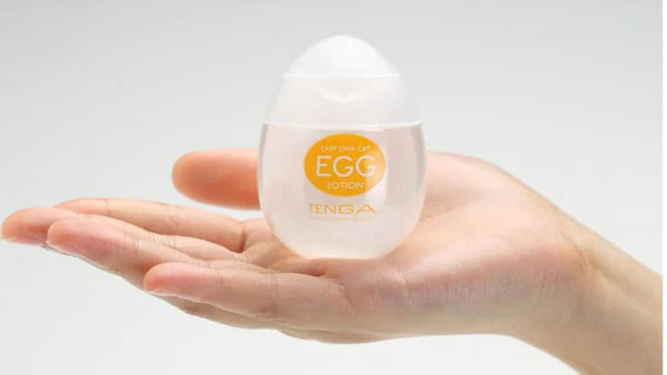 A hand holds a small, egg-shaped bottle of Tenga Egg Lotion lubricant.