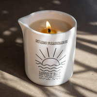 A white ceramic massage candle with a lit wick and "Lovely Day" text.