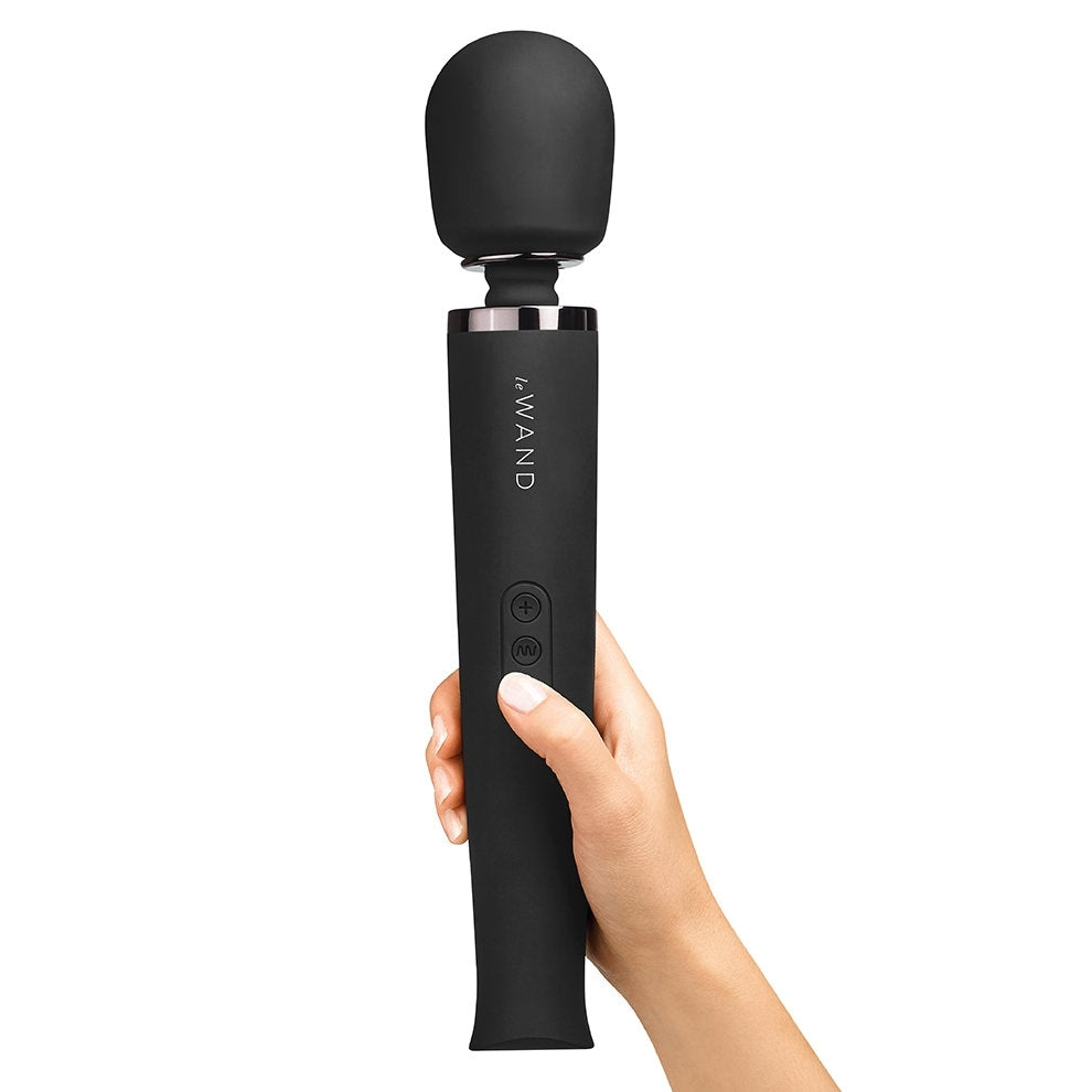 A black rechargeable wand massager with a silicone head held by a hand.