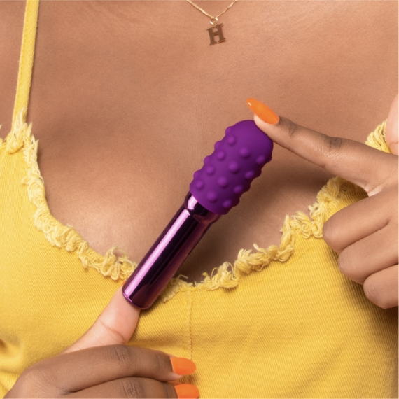 A purple and metallic vibrator held by fingers with orange nails.