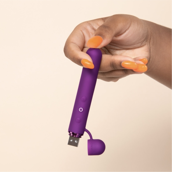 A hand holds a purple mini vibrator with a USB charging port.