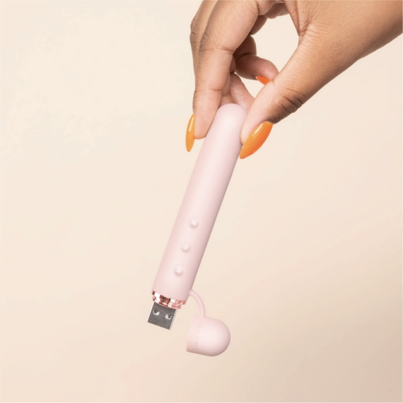 A hand holds a pink mini vibrator with a rose gold USB port.
