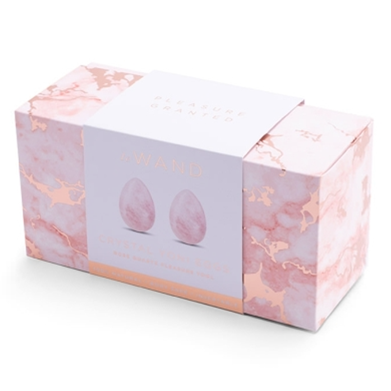 A pink marble box with rose gold accents contains two rose quartz yoni eggs.