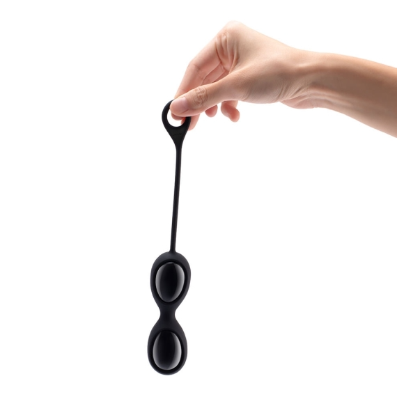 A hand holds a black obsidian yoni egg set with two oval-shaped eggs.