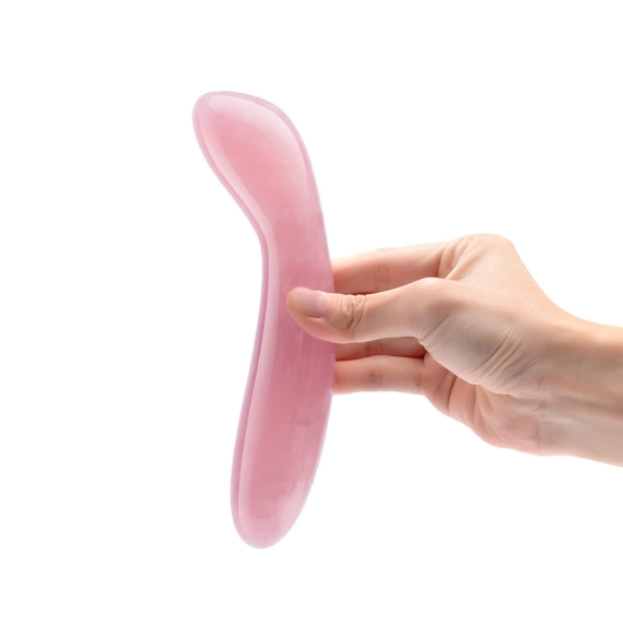 A hand holds a pink rose quartz crystal wand with a curved shape.