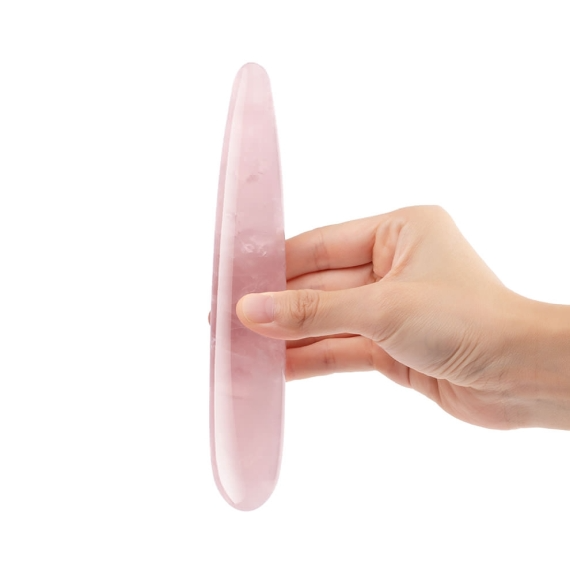 A hand holds a pink rose quartz crystal wand.