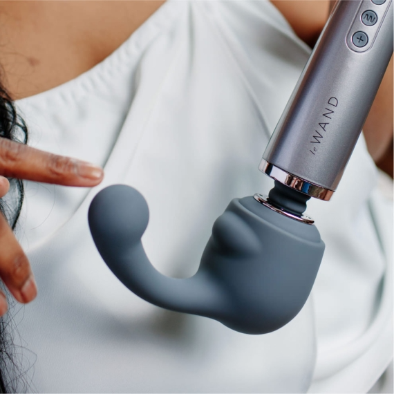 A grey silicone wand attachment with a curved tip is held near a person's chest.
