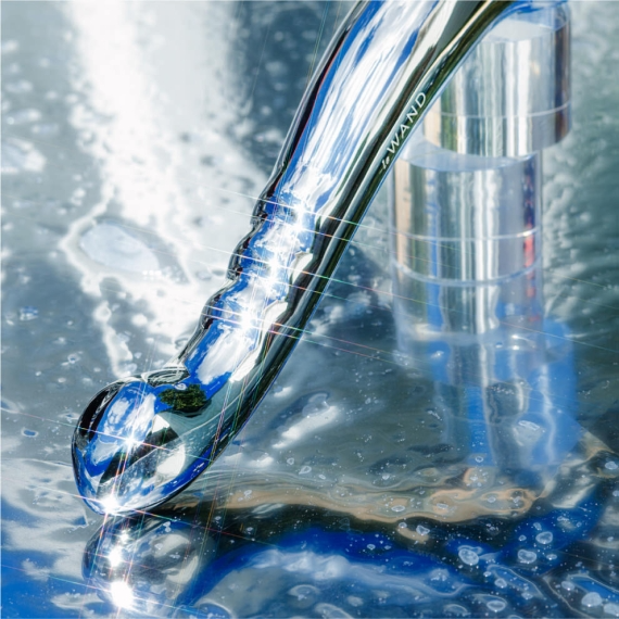 A chrome body wand with a textured grip and rounded tip rests on a reflective surface.