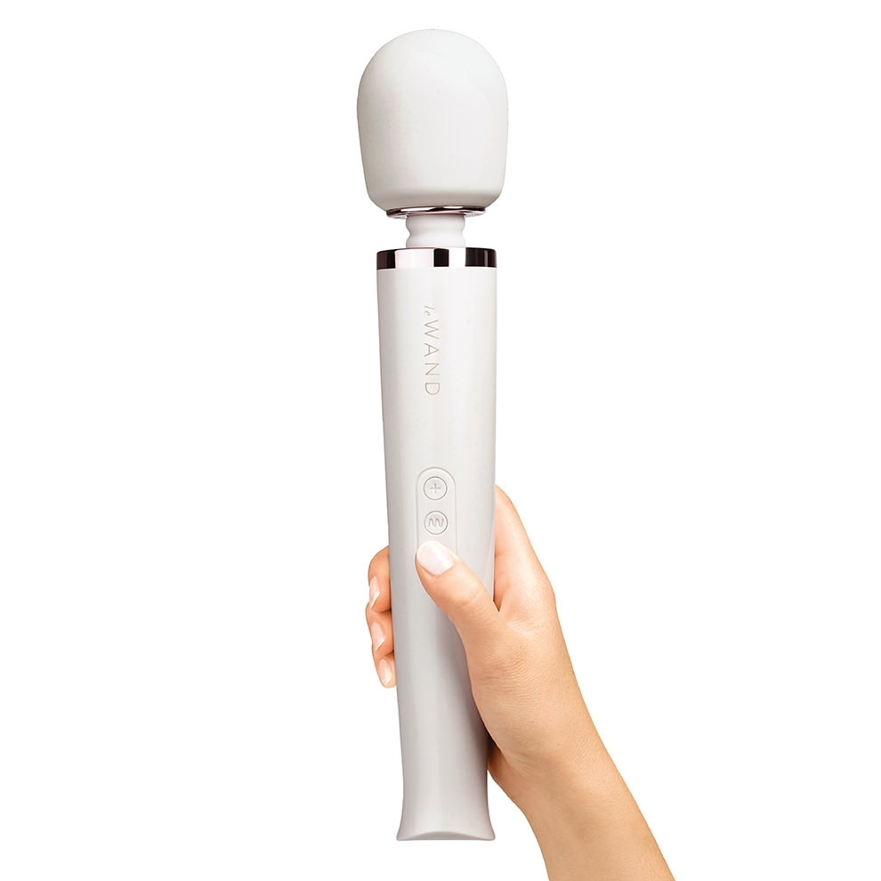 A white rechargeable wand massager held by a hand.