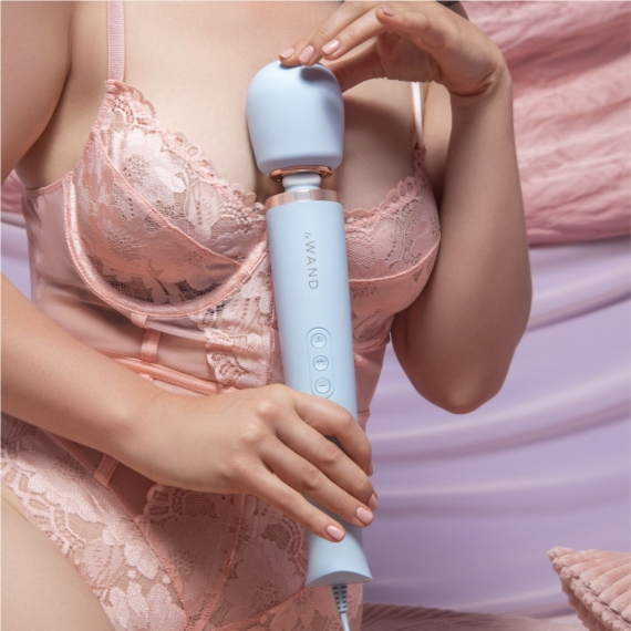 A light blue wand massager with a rose gold accent is held by a person wearing a pink lace corset.