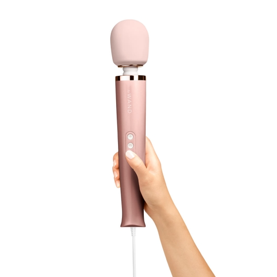 A hand holds a rose gold plug-in wand massager with a pink silicone head.