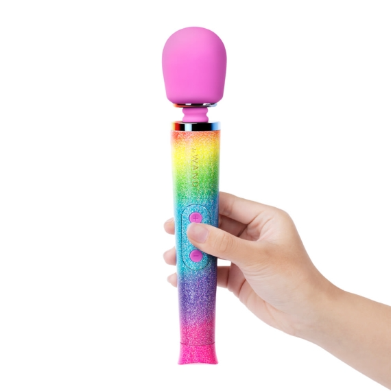 A hand holds a rainbow ombre petite wand massager with a pink silicone head.