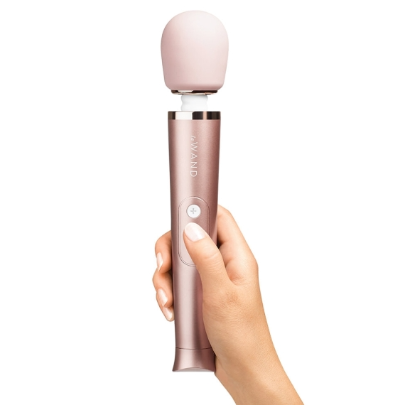 A hand holds a rose gold rechargeable wand vibrator with a pink head.