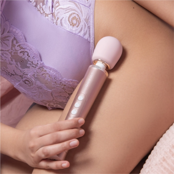 Rose gold Le Wand Petite rechargeable wand vibrator held against a model in purple lingerie.