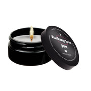 A black massage candle with a lit wick and a lid displaying text.