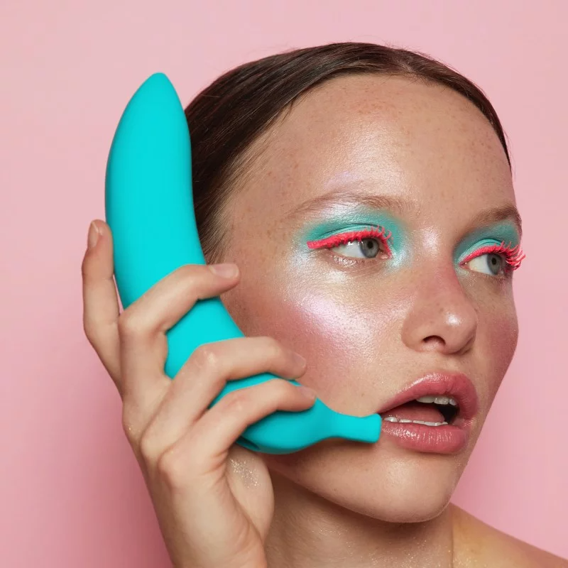 A blue silicone banana vibrator held to a woman's mouth.