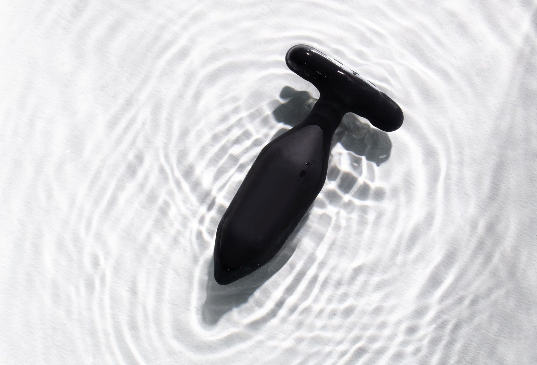 Black vibrating anal plug with a T-shaped handle submerged in water.