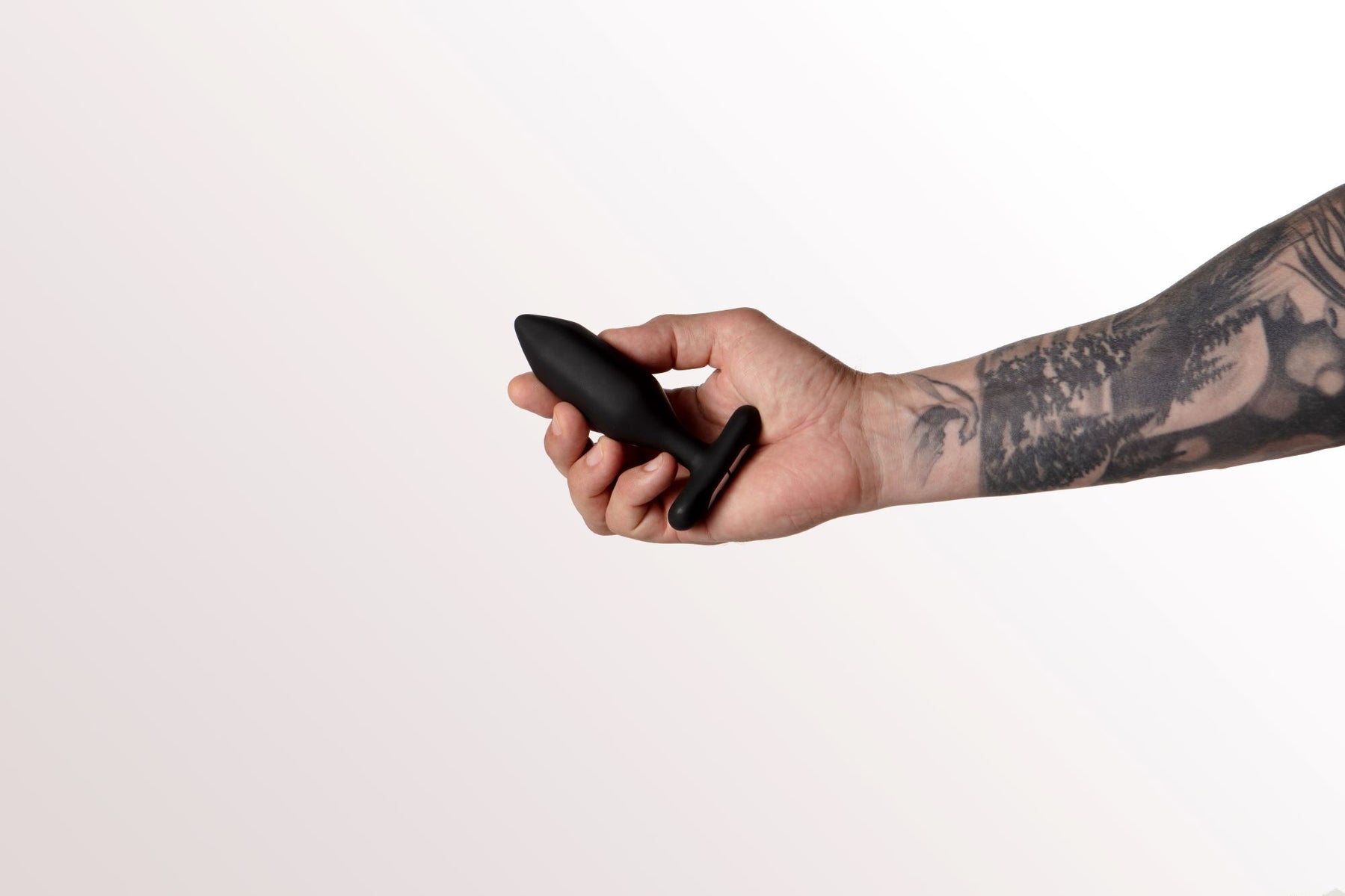 A hand holds a black vibrating anal plug with a T-shaped base.