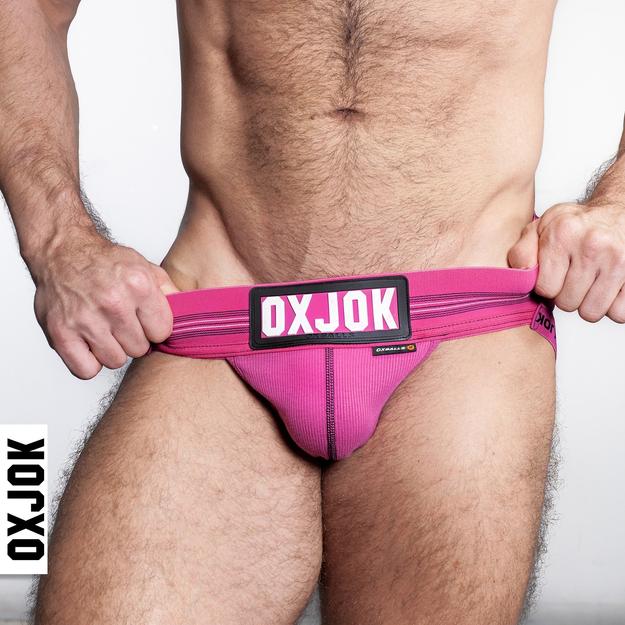 Pink jockstrap with a black and white logo patch and ribbed pouch.