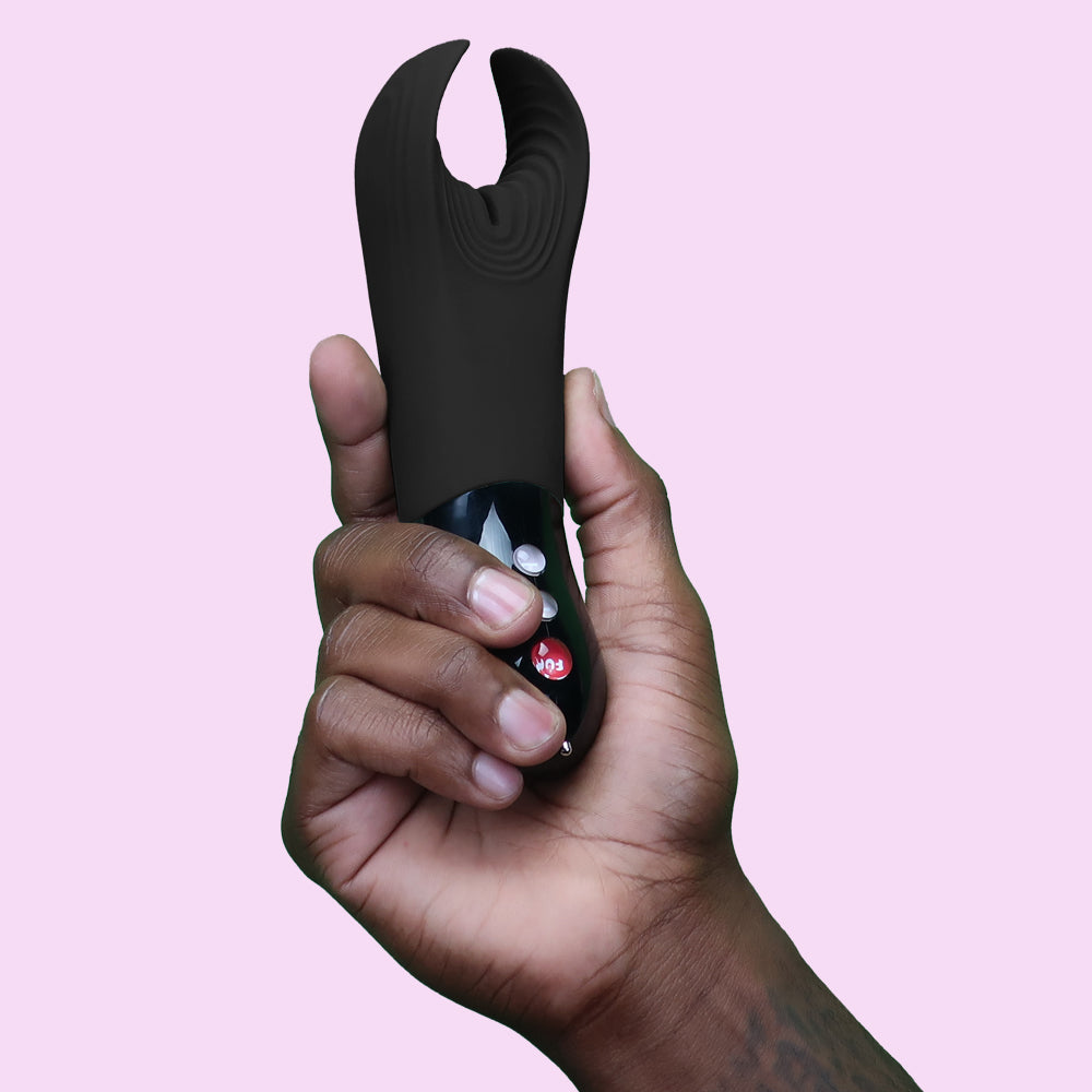 A hand holds a black vibrating pleasure device with red and white buttons.
