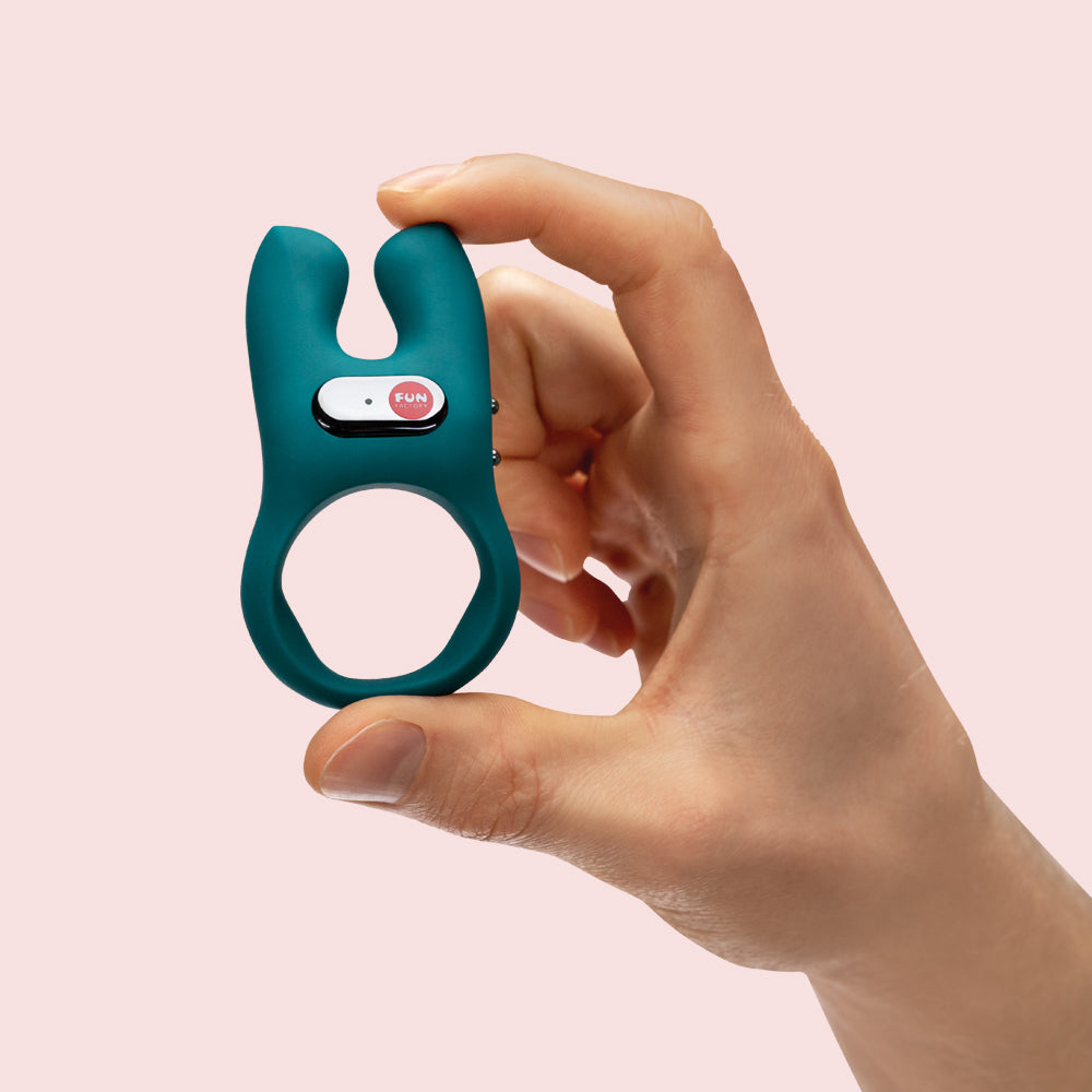 A teal-colored vibrator with a "FUN" button is held in a hand.