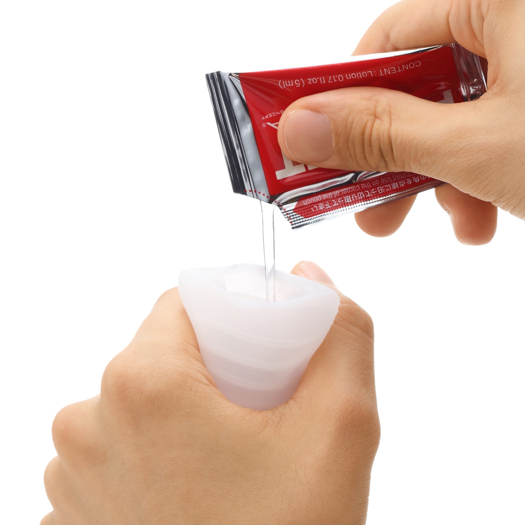 A hand pours liquid from a red packet into a white silicone cup.