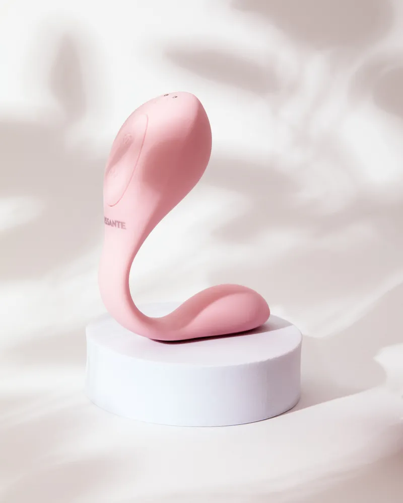 A pink dual stimulation vibrator with suction on a white pedestal.