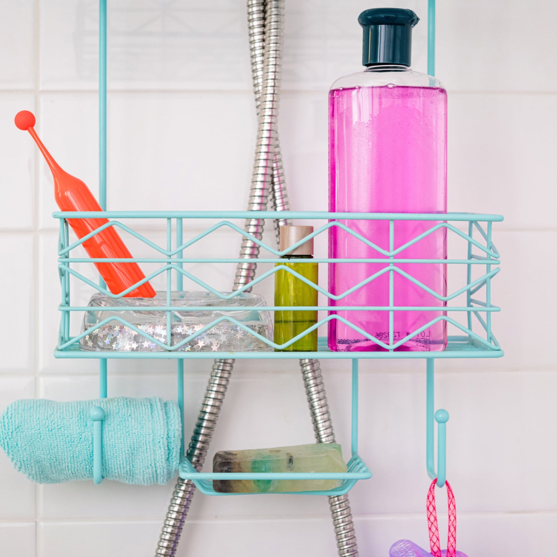 A teal shower caddy holds a pink bottle of liquid, a small green bottle, a toothbrush, a bar of soap, and a folded towel.