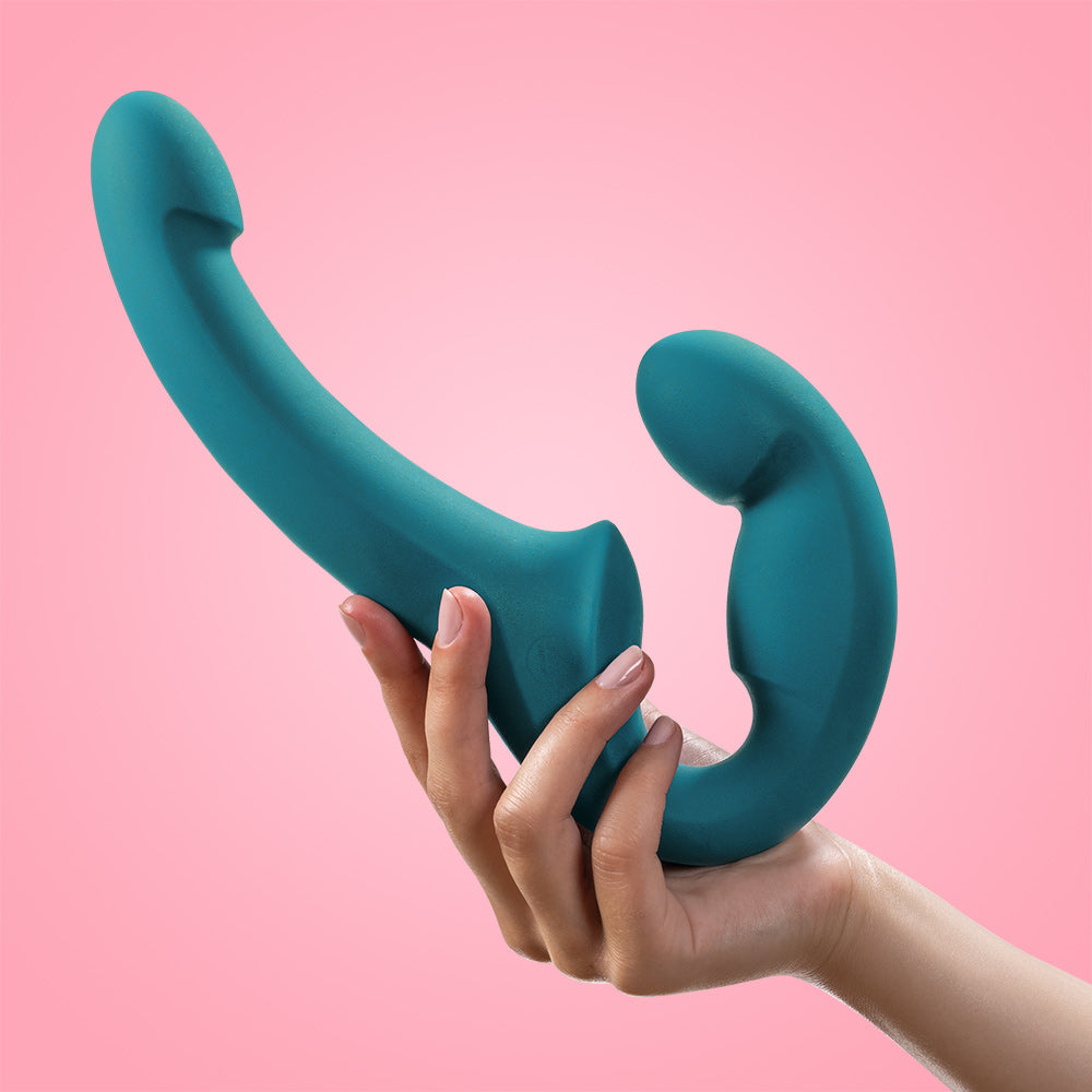 A teal double-ended dildo with a curved shape is held in a hand.