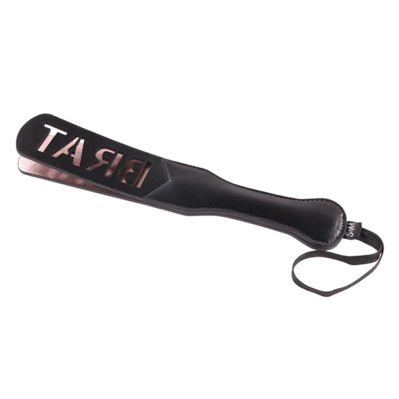 Black faux leather spanking paddle with rose gold "BRAT" cutouts and a wrist strap.