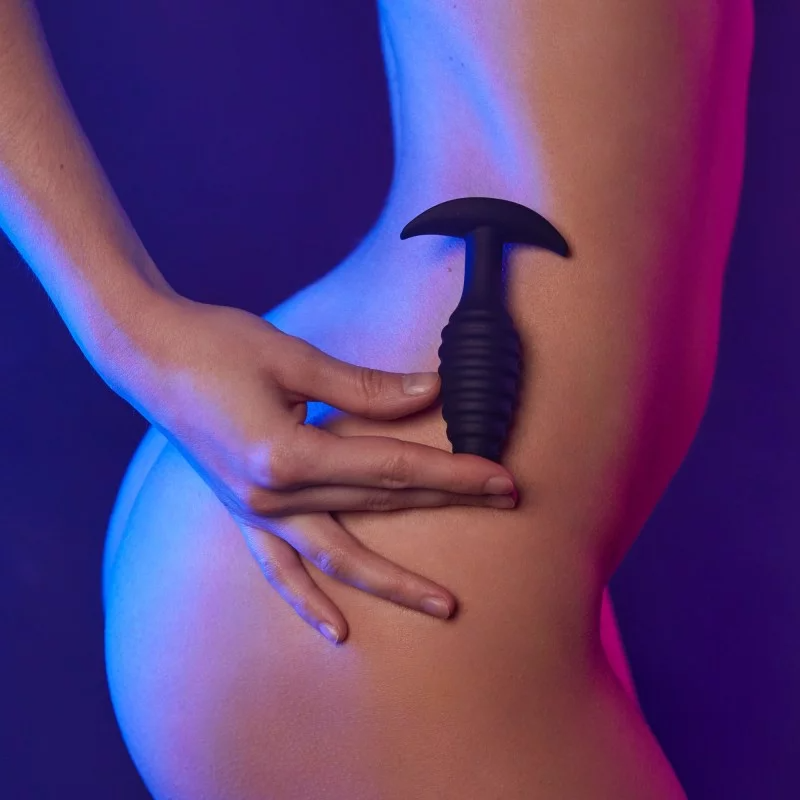 Black textured silicone anal plug held against skin.