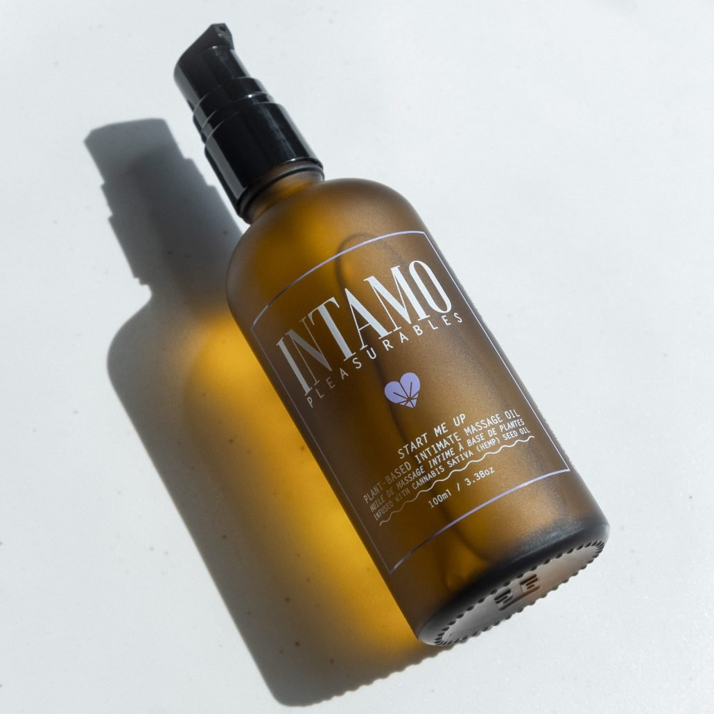 A brown glass bottle of Intamo intimate massage oil with a black pump dispenser.