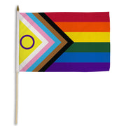 Inclusive Pride stick flag with rainbow and progress stripes on a wooden pole.