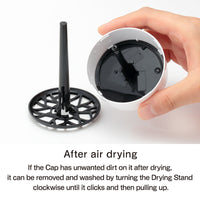 A hand holds a white Tenga masturbator with a black drying stand.