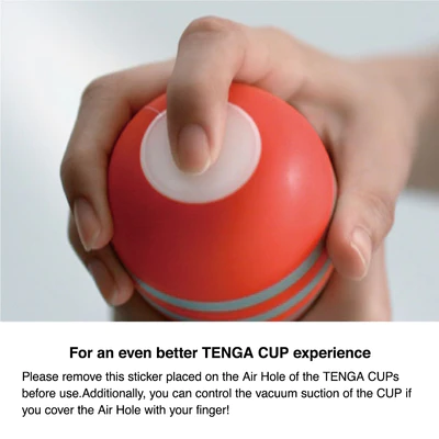 A hand holds a red Tenga vacuum cup with a white air hole.