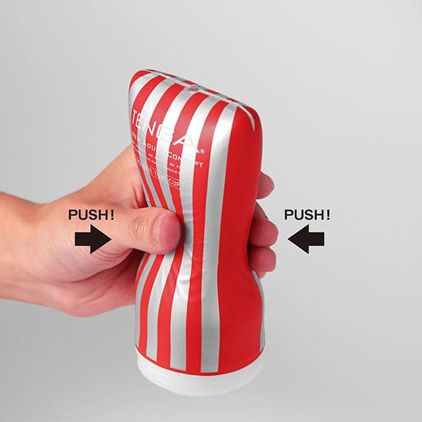 A hand squeezes a red and silver striped Tenga soft tube cup masturbator.