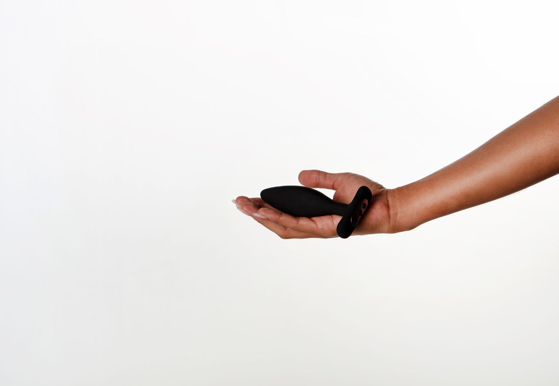 A black vibrating butt plug with a flared base rests in an open hand.