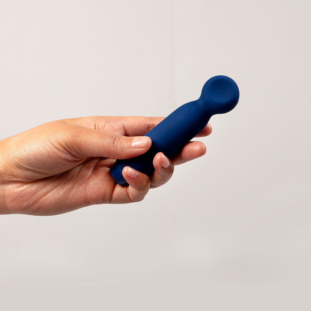 A hand holds a cobalt blue vibrating bullet with a rounded tip.