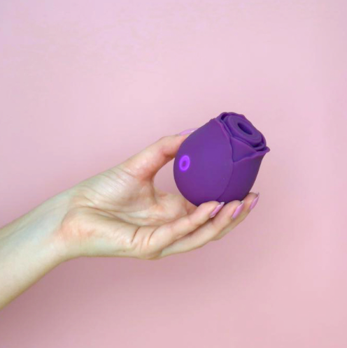 A purple rose-shaped massager with a glowing button held in a hand.