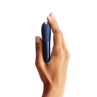 A hand holds a midnight blue rechargeable ball vibrator with two buttons.